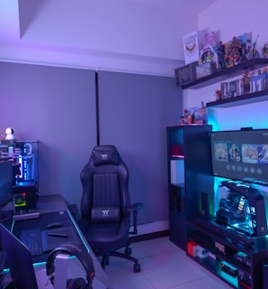 A modern gaming setup featuring a sleek gaming chair, dual monitors on a desk, and LED lighting. A gaming console and various decorations are displayed on shelves, creating an organized and vibrant gaming environment.