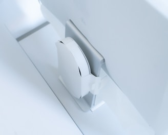 A white, sleek, vertical gaming console placed beside a large, slim monitor. The setting exudes minimalism with a focus on modern technology design.