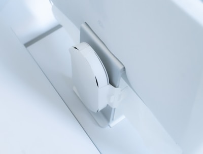 A white, sleek, vertical gaming console placed beside a large, slim monitor. The setting exudes minimalism with a focus on modern technology design.