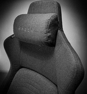 A high-quality, fabric gaming chair featuring ergonomic design and enhanced comfort. The chair has a distinct headrest with visible stitching, embossed branding, and a modern aesthetic.